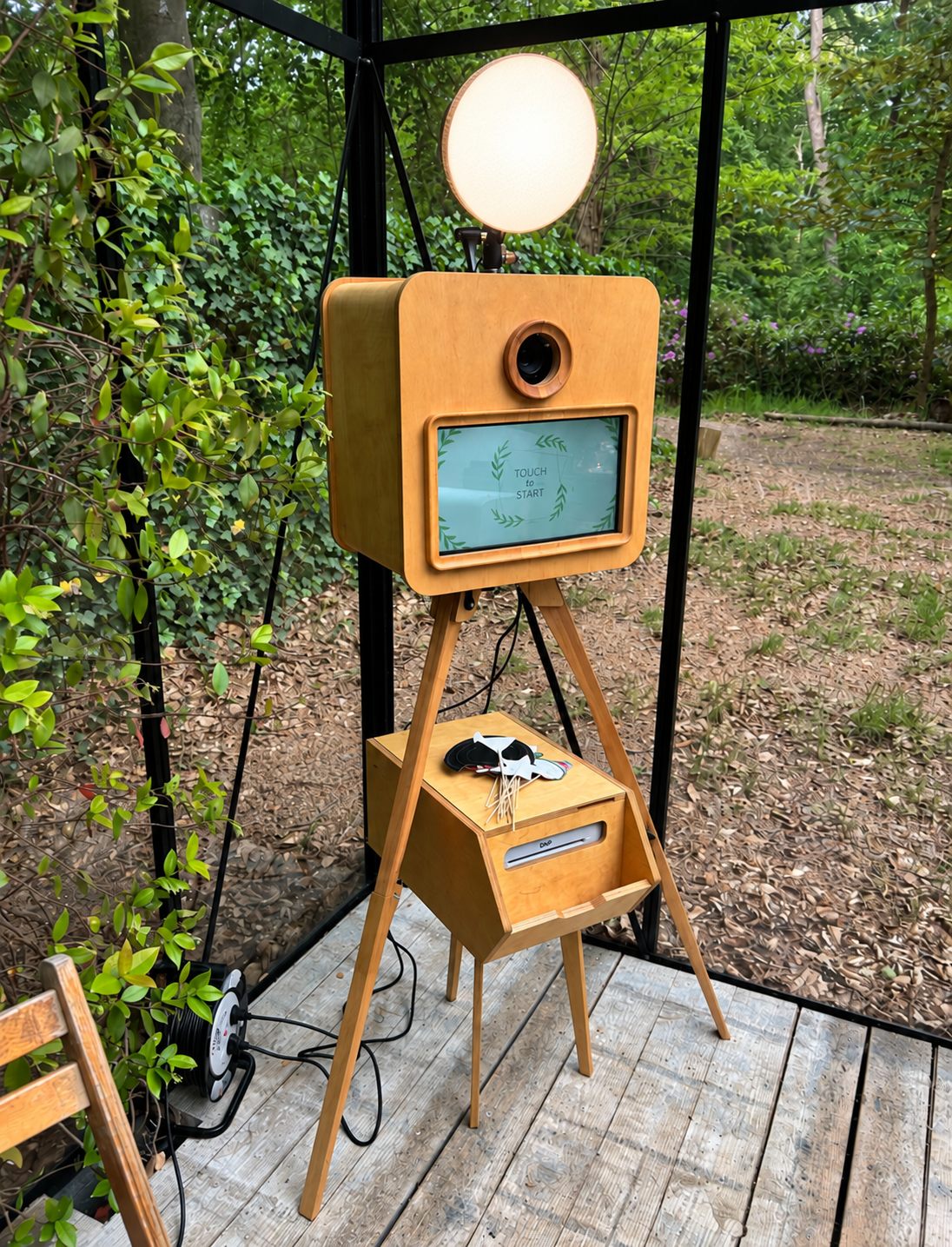 De houten photobooth met softbox, touchscreen, props en printer in een tuinkamer